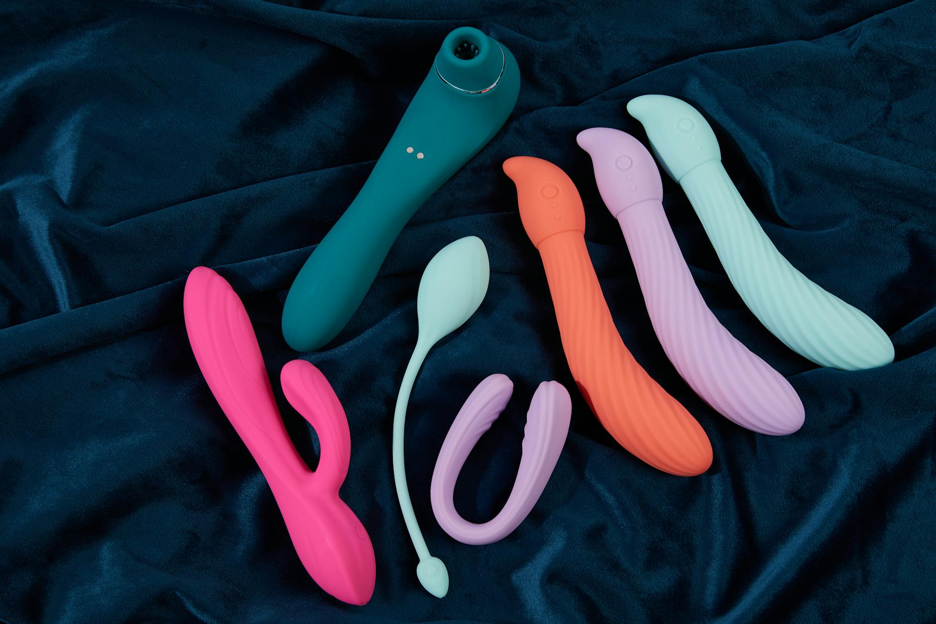 A blue silicone clitoral vibrator held gently in hand against a purple background