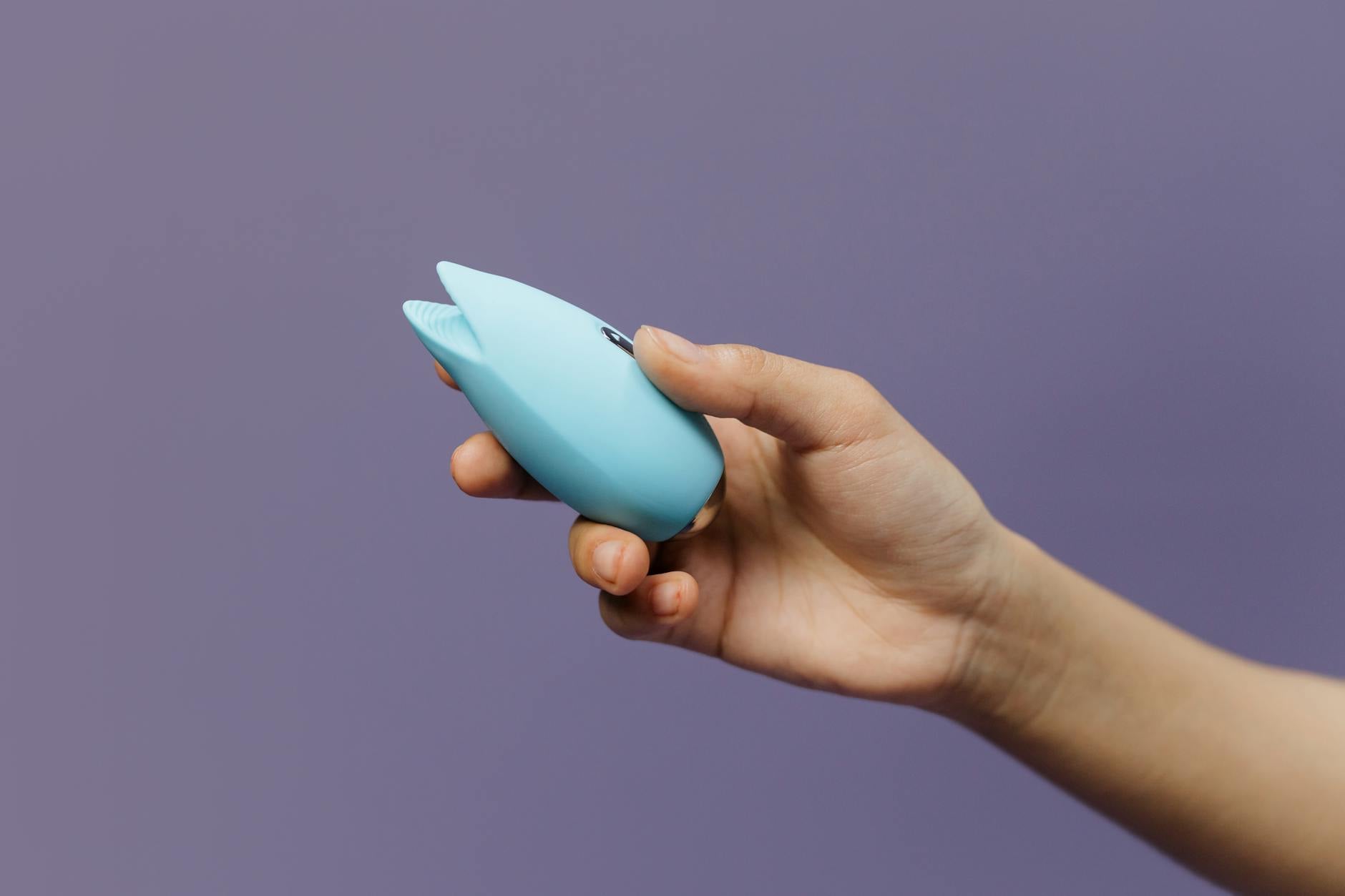 A silicone clitoral vibrator held in hand against a purple background, promoting self-care and pleasure