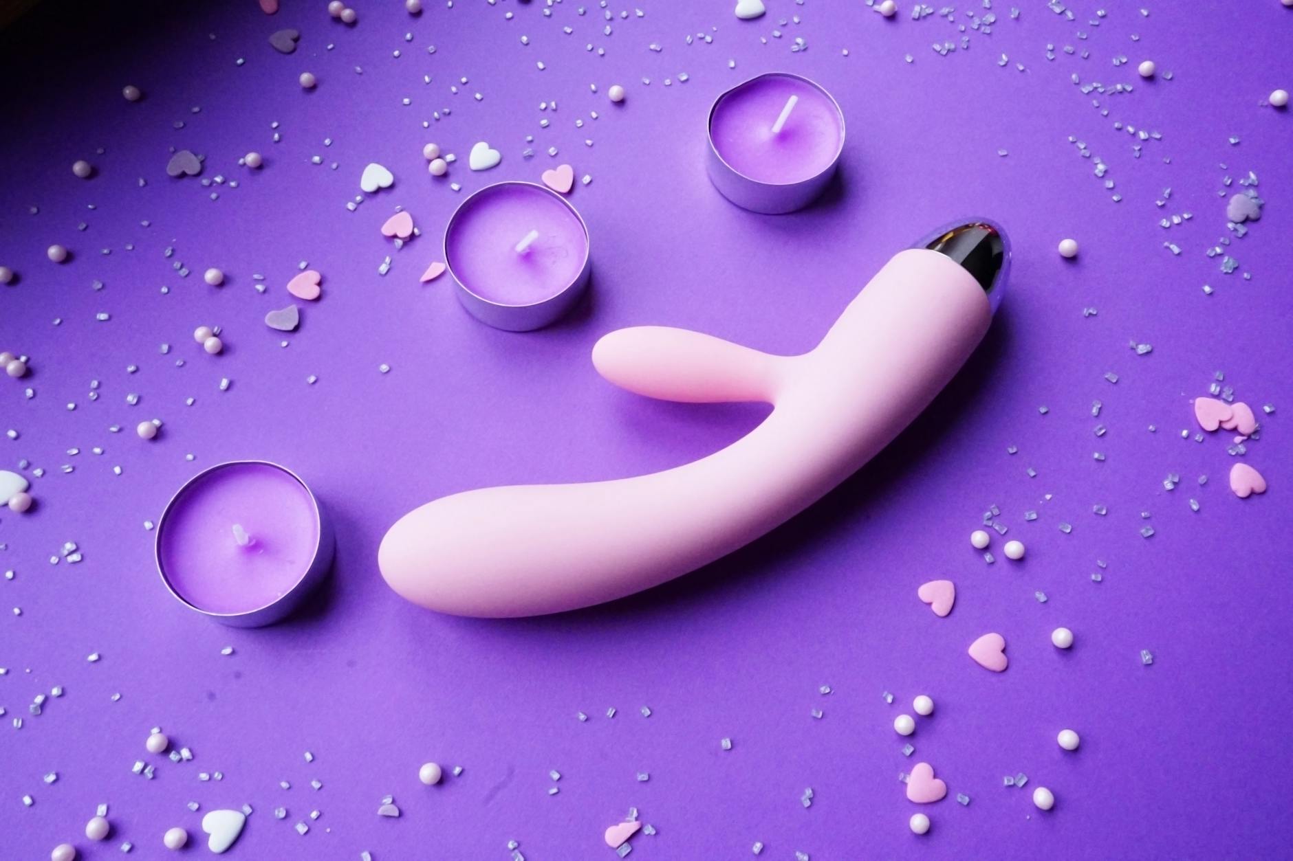 A vibrator surrounded by candles and rose petals on a soft pink surface, symbolizing reconnection and intimacy.